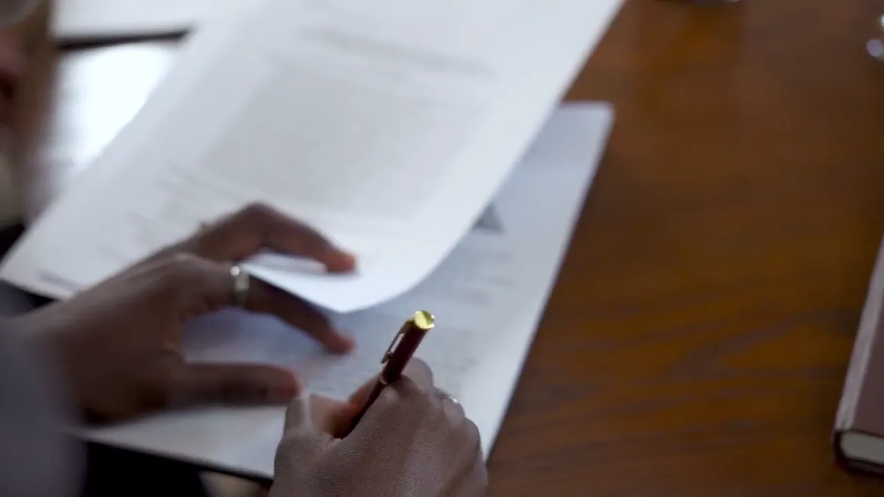 A person reviews and signs printed papers at a wooden desk.